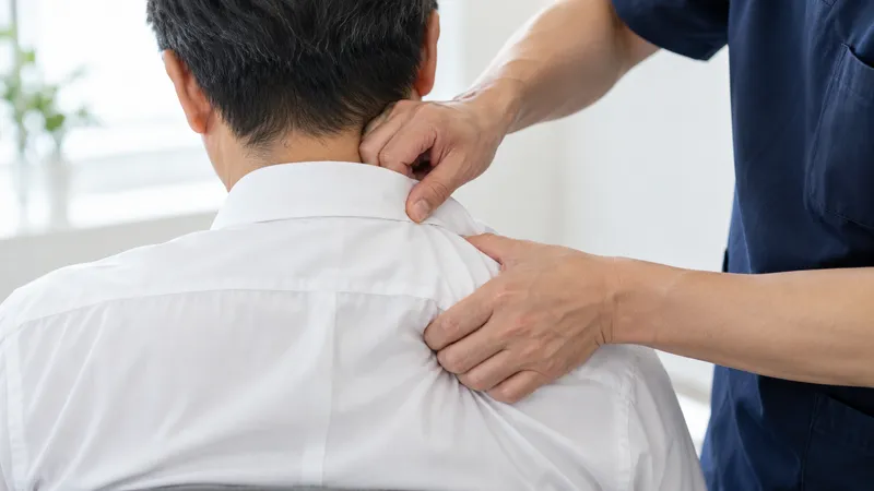 施術者がワイシャツ姿の男性の首と肩をほぐす手元