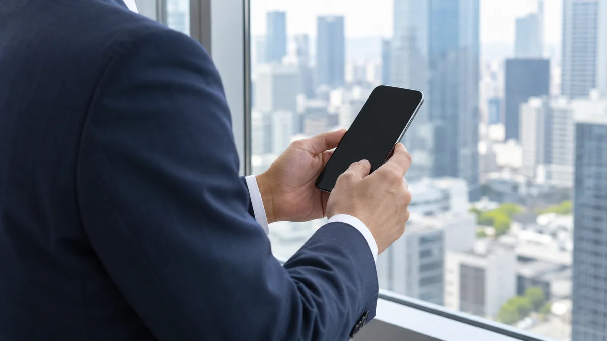 窓辺でスマートフォンを見るスーツ姿の男性の手元